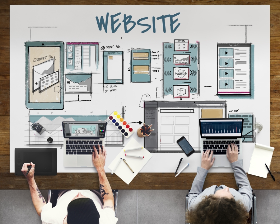 A picture of 2 people from above sitting at a table with complex drawings of systems to design a website to represent Kazzicom's web design and hosting services, along with the word 'website'